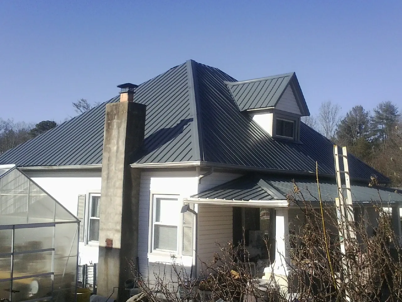 Dark blue standing seam metal roof on a white farmhouse with dormer — Slate & Tile Roof Repair by Roofing Brothers in Gladbrook