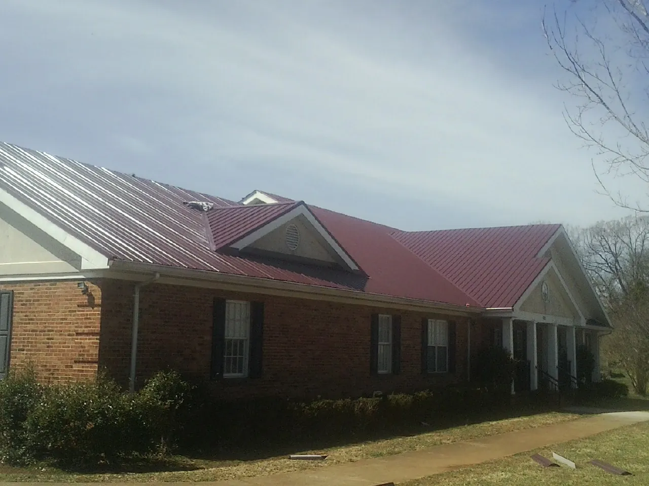 Red metal roof with gabled entries on a long brick building, from a Hail Damage Roof Repair job in Gladbrook
