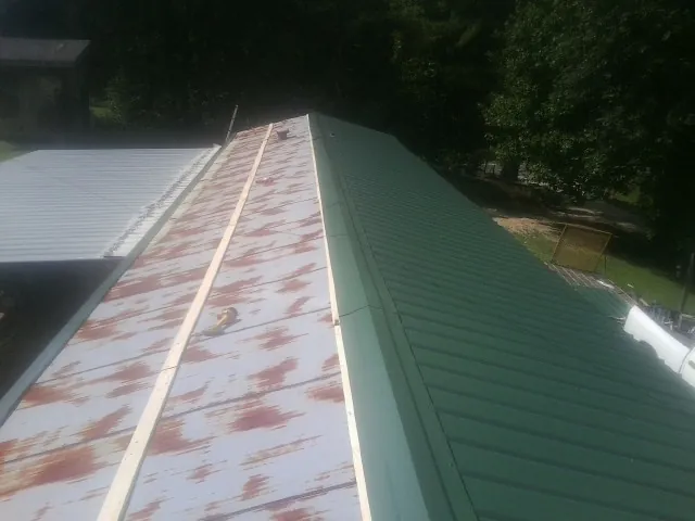 Old rusted panels beside newly installed green metal roofing — Wind Damage Roof Repair by Roofing Brothers in Gladbrook