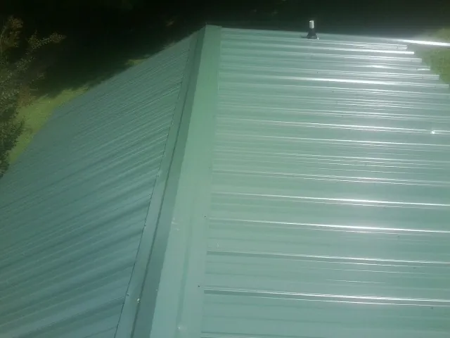 New green metal panels meeting at the ridge of a roof — Flat Roof Repair work by our crew in Gladbrook