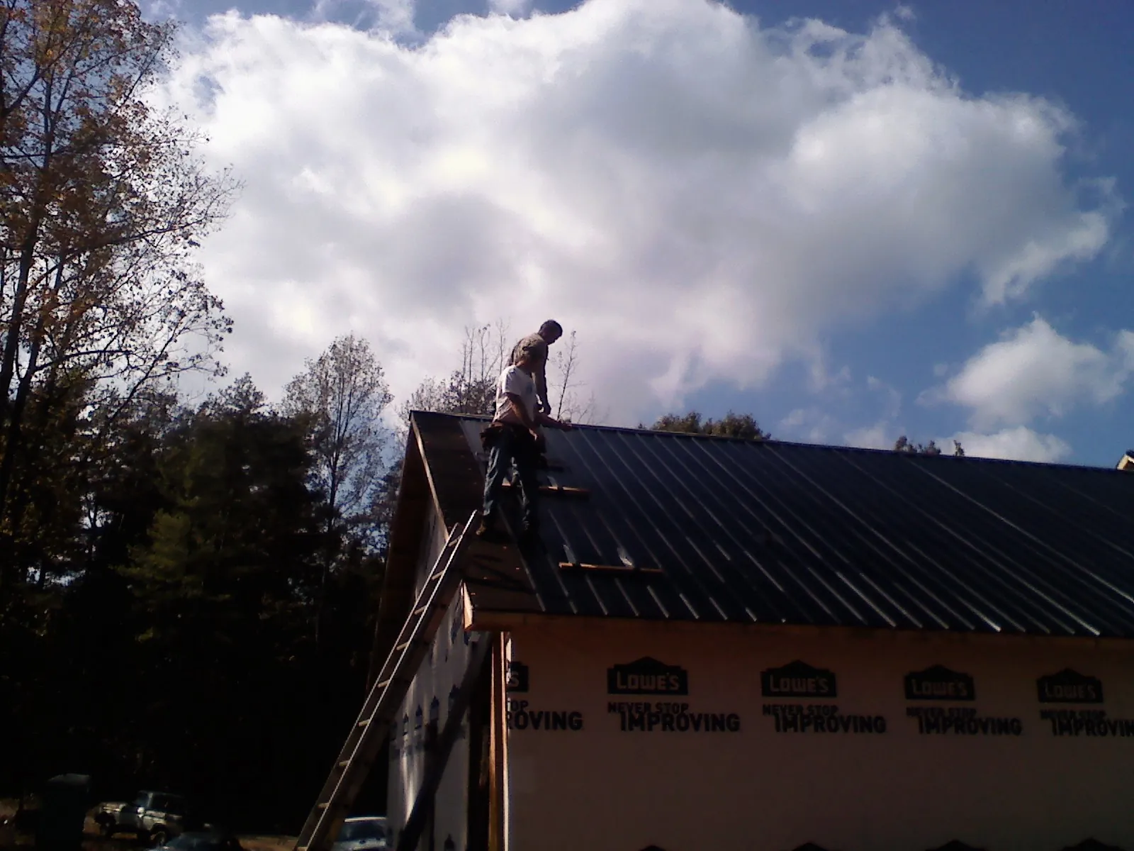 Roofer fastening dark metal panels high against a cloudy sky, from a Roof Inspection job in Gladbrook