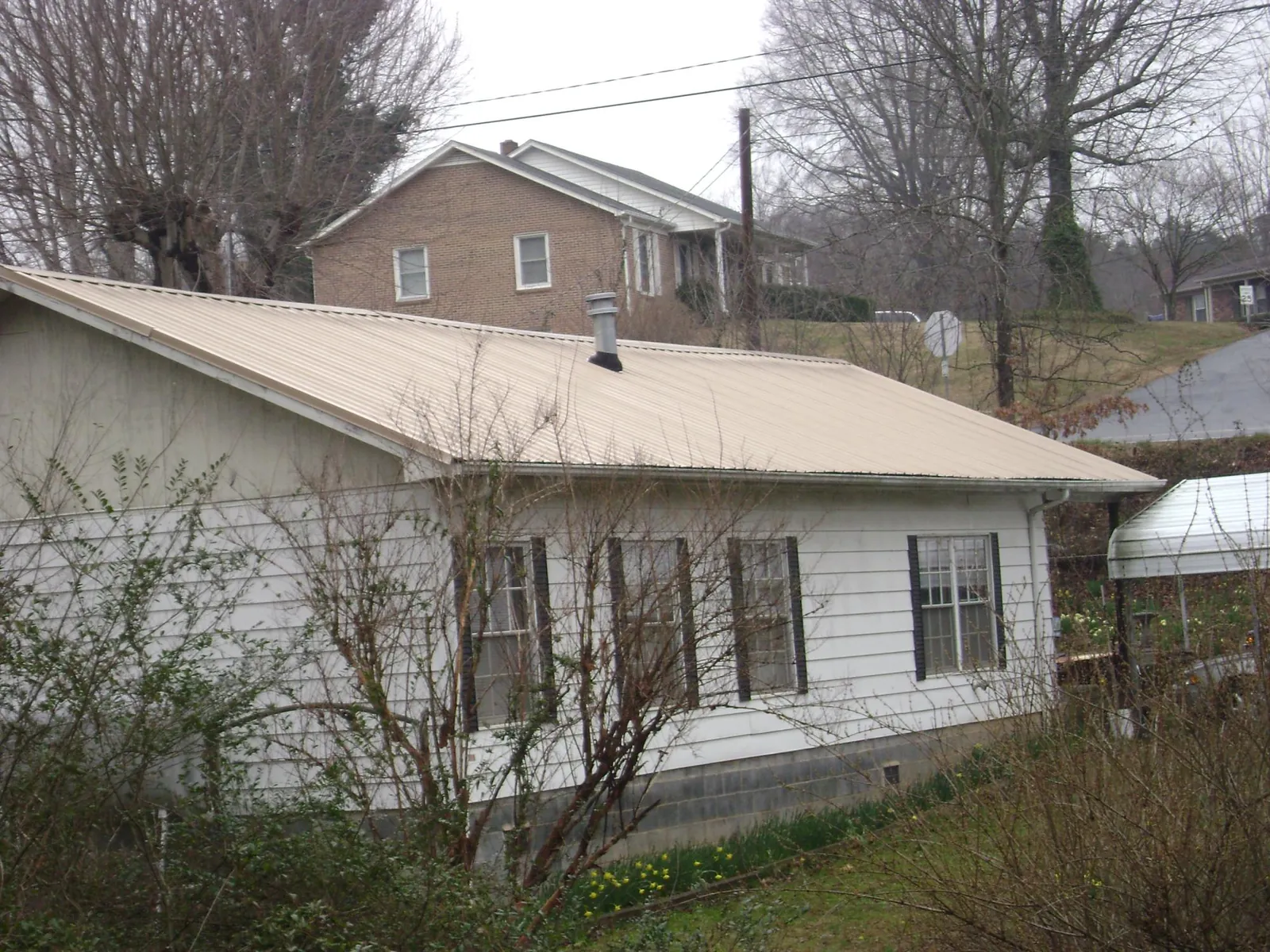 Tan metal roof on a white sided house set into a hillside — Commercial Roofing by Roofing Brothers in Gladbrook